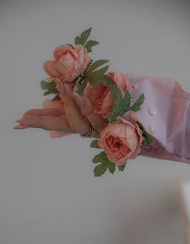 A graceful hand wearing a pink sleeve gently holds pink roses with lush green leaves.