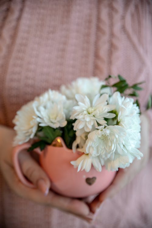 A person holding a pink sweater with white flowers in a mug
