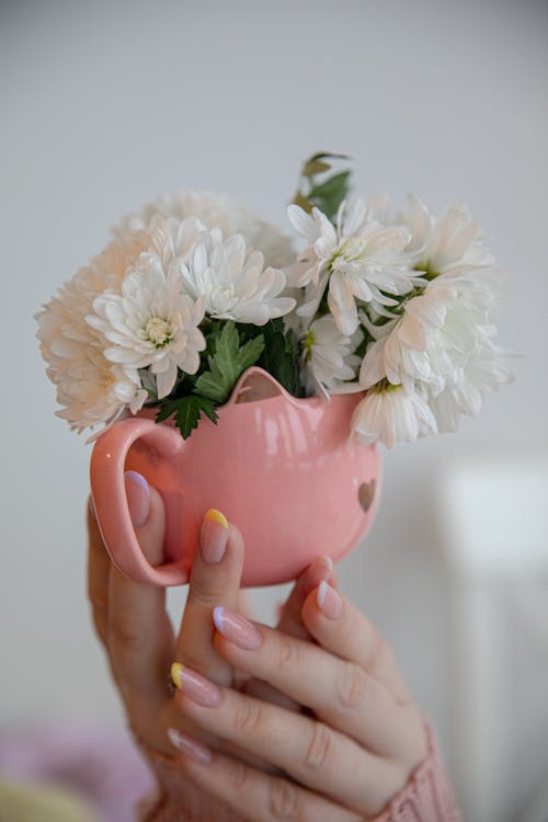 A person holding a pink mug with white flowers in it