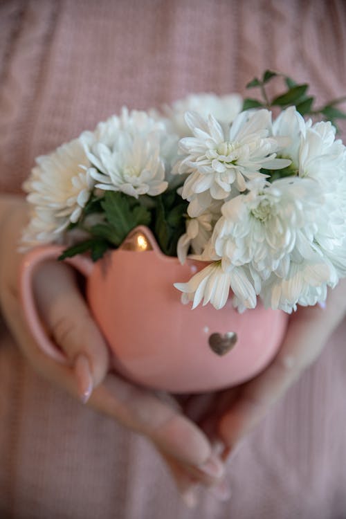 A person holding a pink mug with white flowers in it