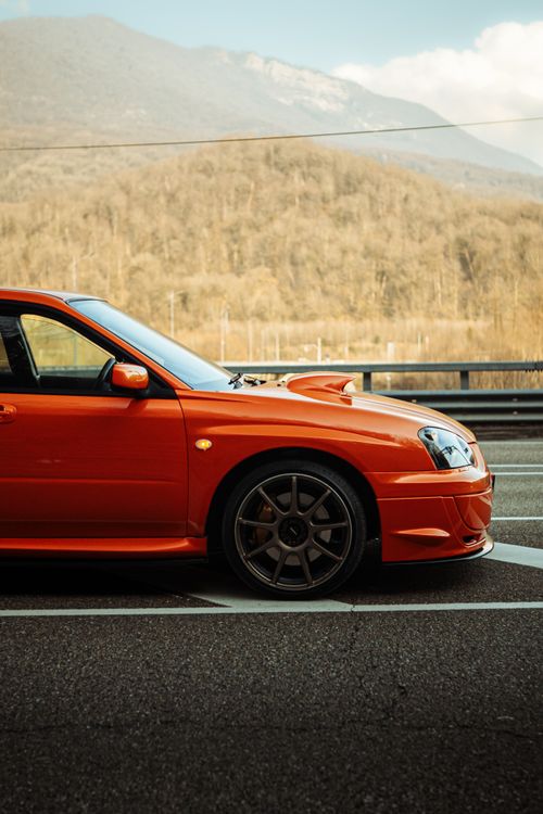 Free A striking red Subaru Impreza parked on a scenic road with mountains in the background. Stock Photo