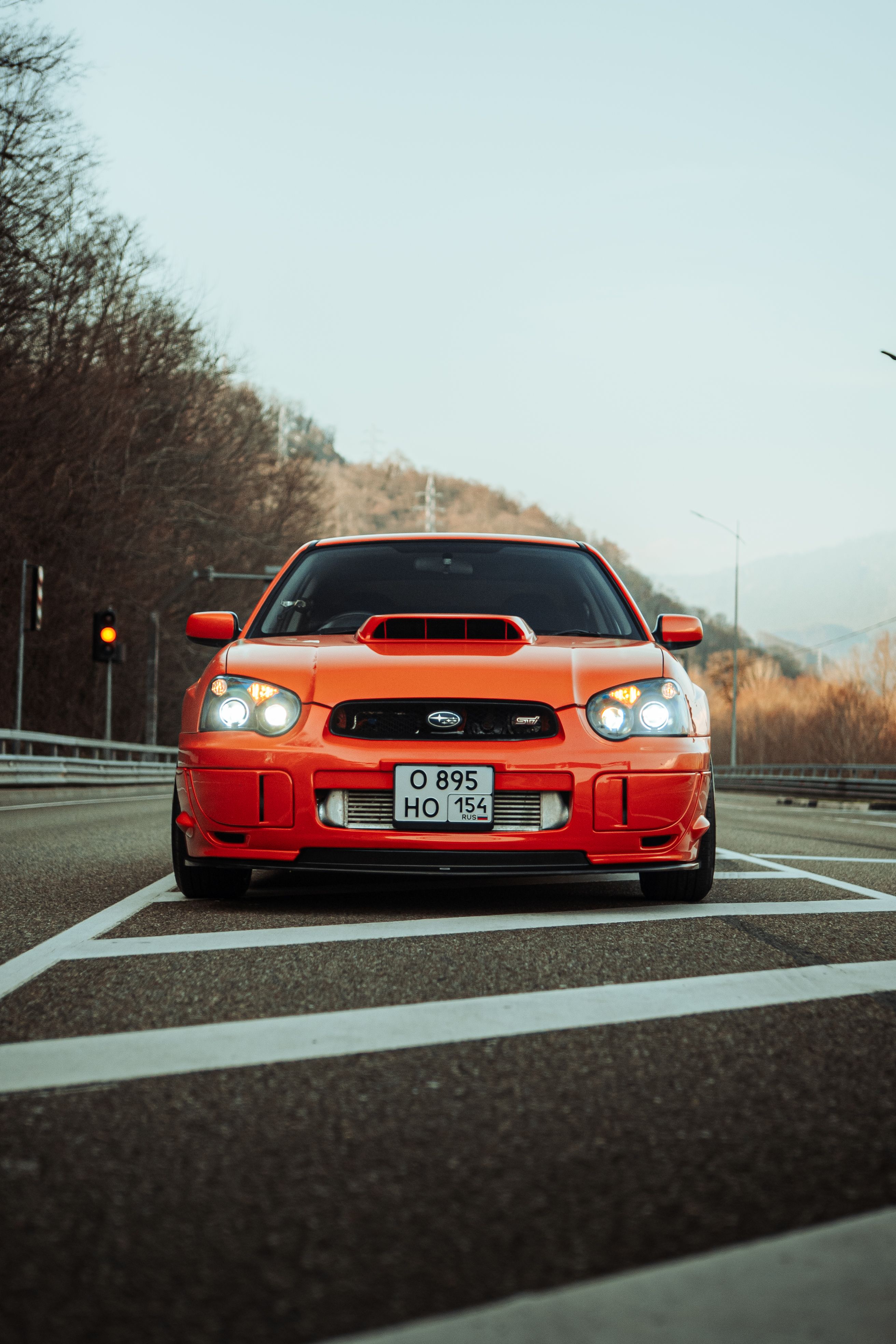 A vibrant red Subaru sports car on an empty scenic highway set against mountainous backdrop.