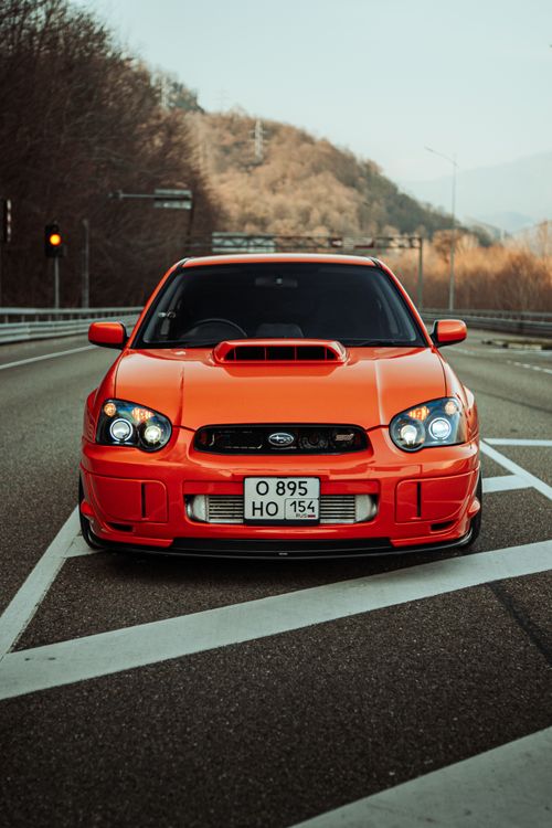 Free Vibrant red Subaru Impreza captured on a scenic highway with mountain backdrop. Stock Photo