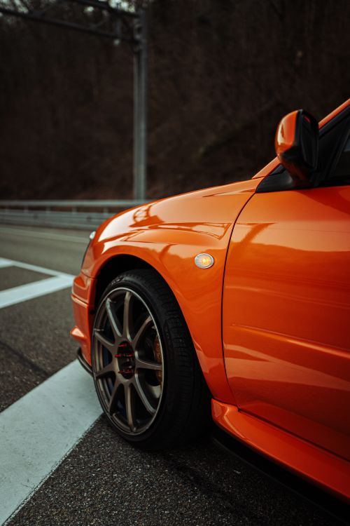 Free Detailed close-up shot of a vibrant orange sports car on a city street, showcasing intricate wheel design. Stock Photo