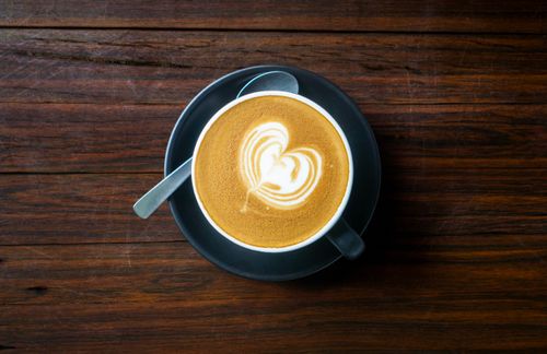 Free A beautifully crafted latte with heart shaped froth art in a cup on a rustic wooden table. Stock Photo