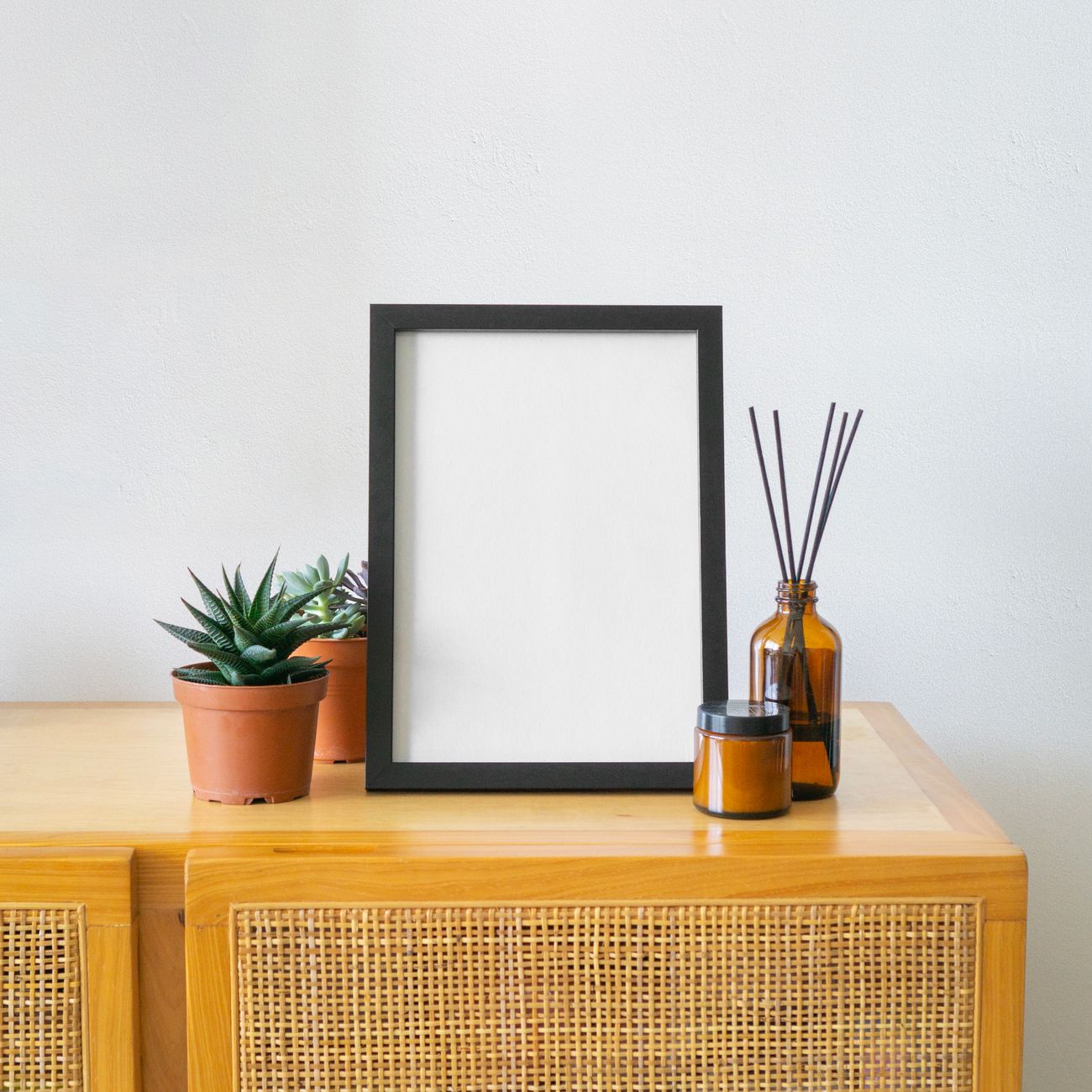 Modern minimalist setup with blank frame and succulents on wooden cabinet.