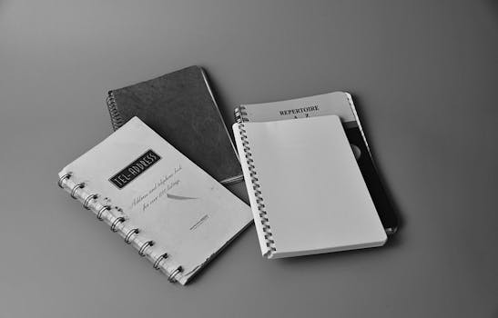 Black and white photo showing spiral notebooks with cover texts in a flat lay setup.