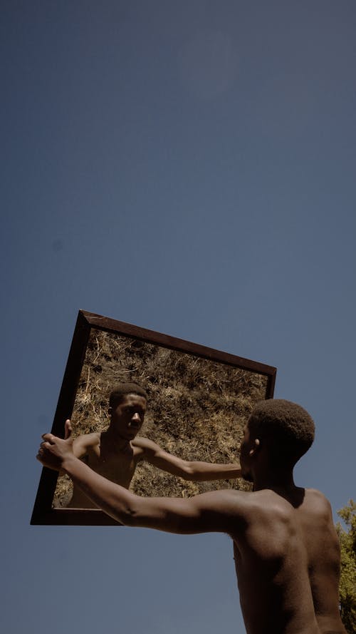 Back of a Shirtless Man Holding a Mirror against the Clear Sky