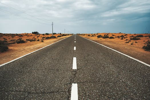 阿联酋迪拜，一条笔直空旷的沙漠道路延伸在多云的天空下，凸显出孤独与广阔