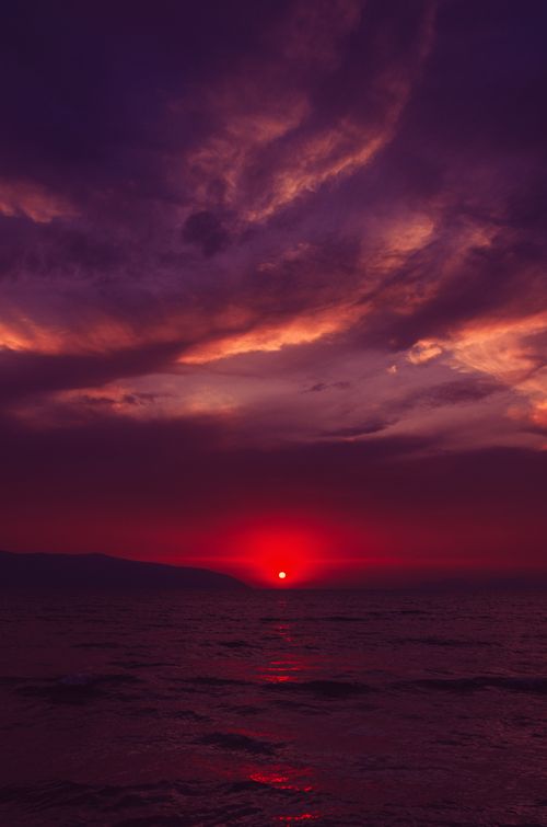 Free A vibrant sunset over the sea with a dramatic purple and red sky. Stock Photo