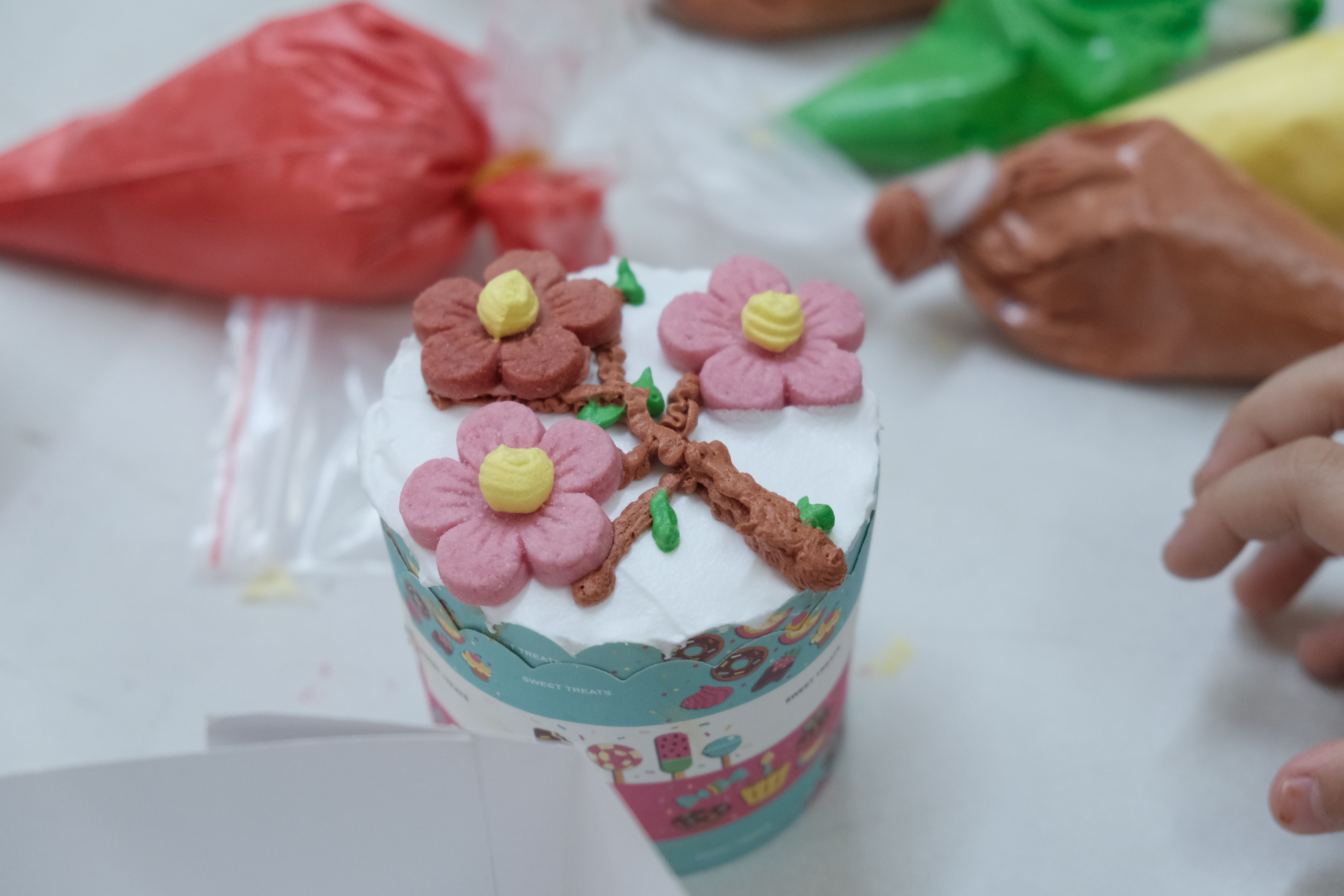Close-up of a cupcake with floral frosting design and colorful icing bags.