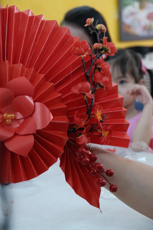 A person holding a red paper fan with red flowers