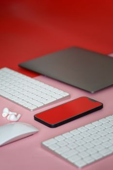 Stylish flat lay of modern gadgets including a smartphone, keyboard, and mouse on a red background.