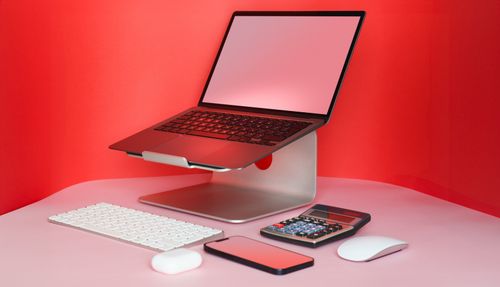 Free Sleek modern workspace with a laptop, keyboard, mouse, and calculator in a vibrant red setting. Stock Photo