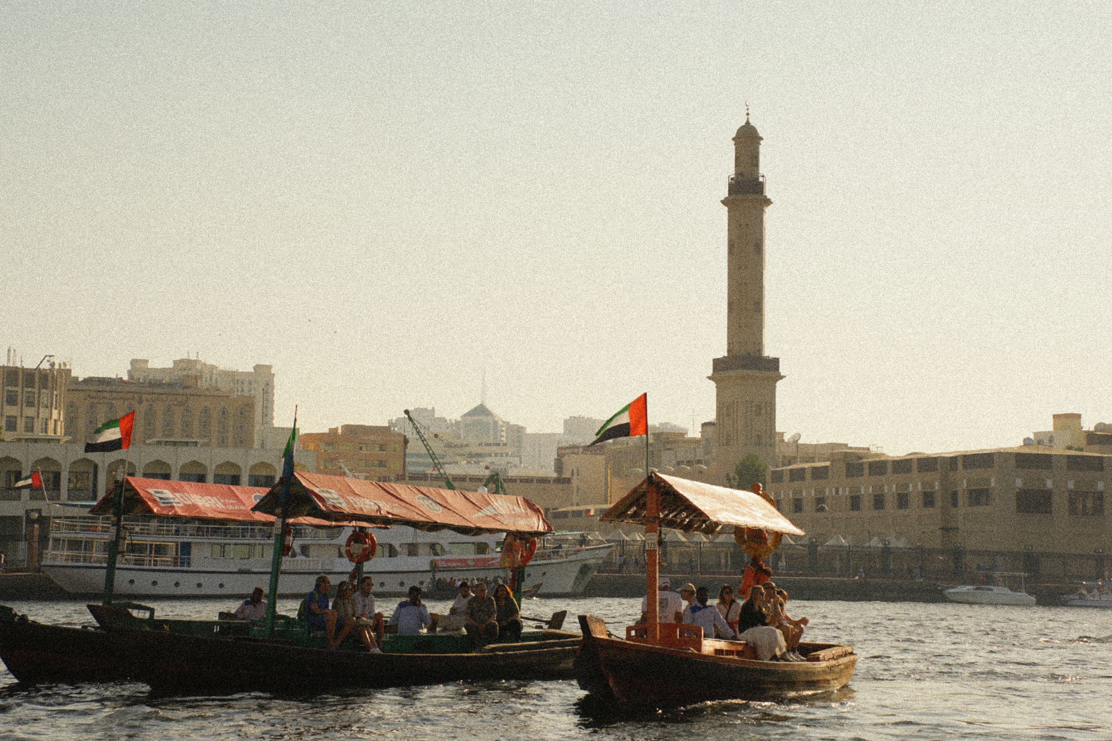 Traditional boats on a bustling Dubai waterway with cityscape and minaret view.