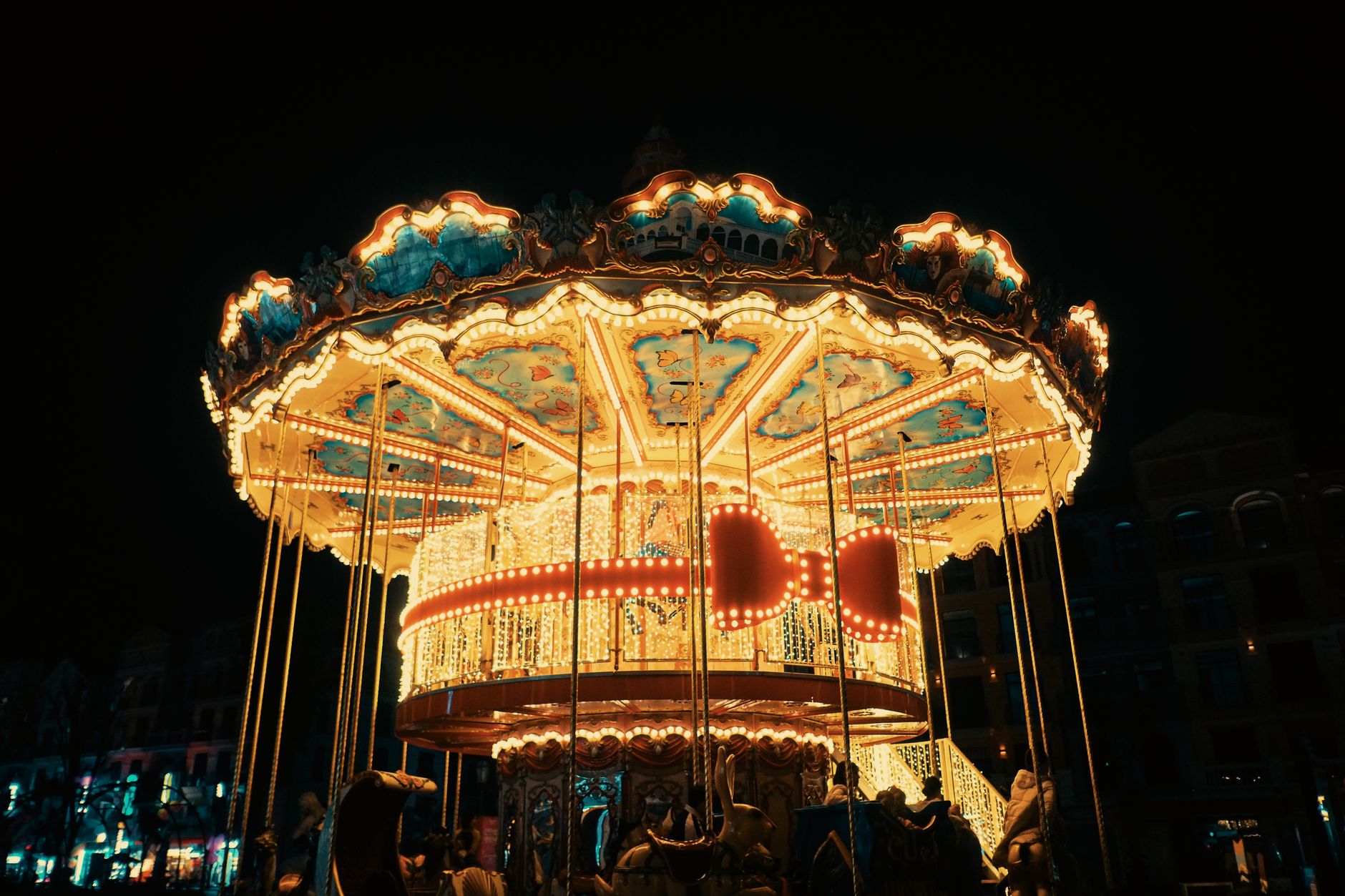 A beautifully lit carousel spinning at a nighttime carnival, creating a vibrant, festive atmosphere.