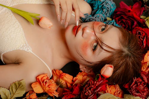 A woman laying on top of flowers with a flower in her mouth