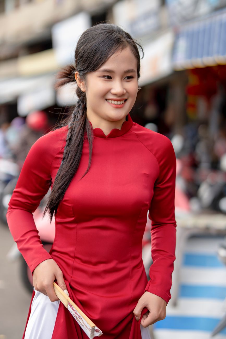 Young woman in red traditional dress smiling on bustling city street.