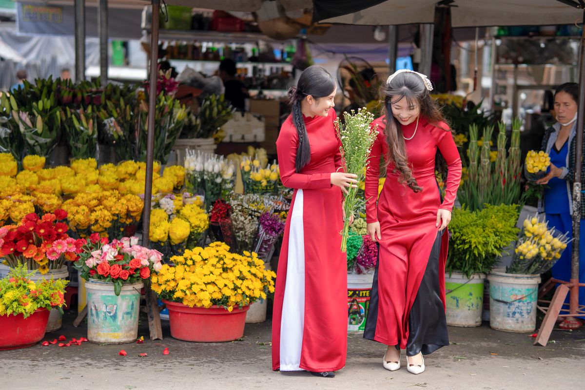 Hai cô gái mặc áo dài đỏ dạo chợ hoa, một người cầm bó hoa trắng