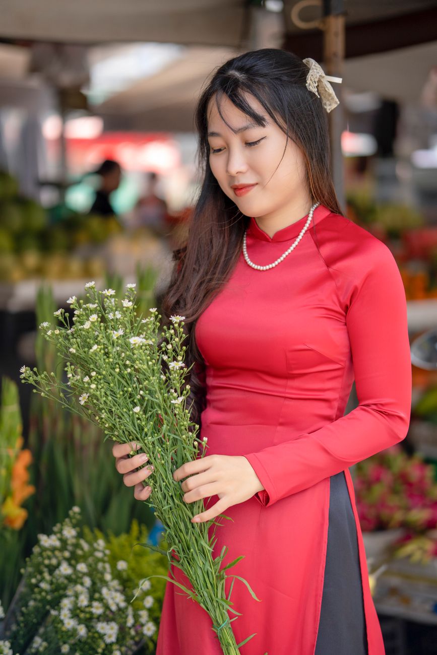 Portrait of a young woman in a vibrant red dress holding white flowers, reflecting cultural elegance and grace.