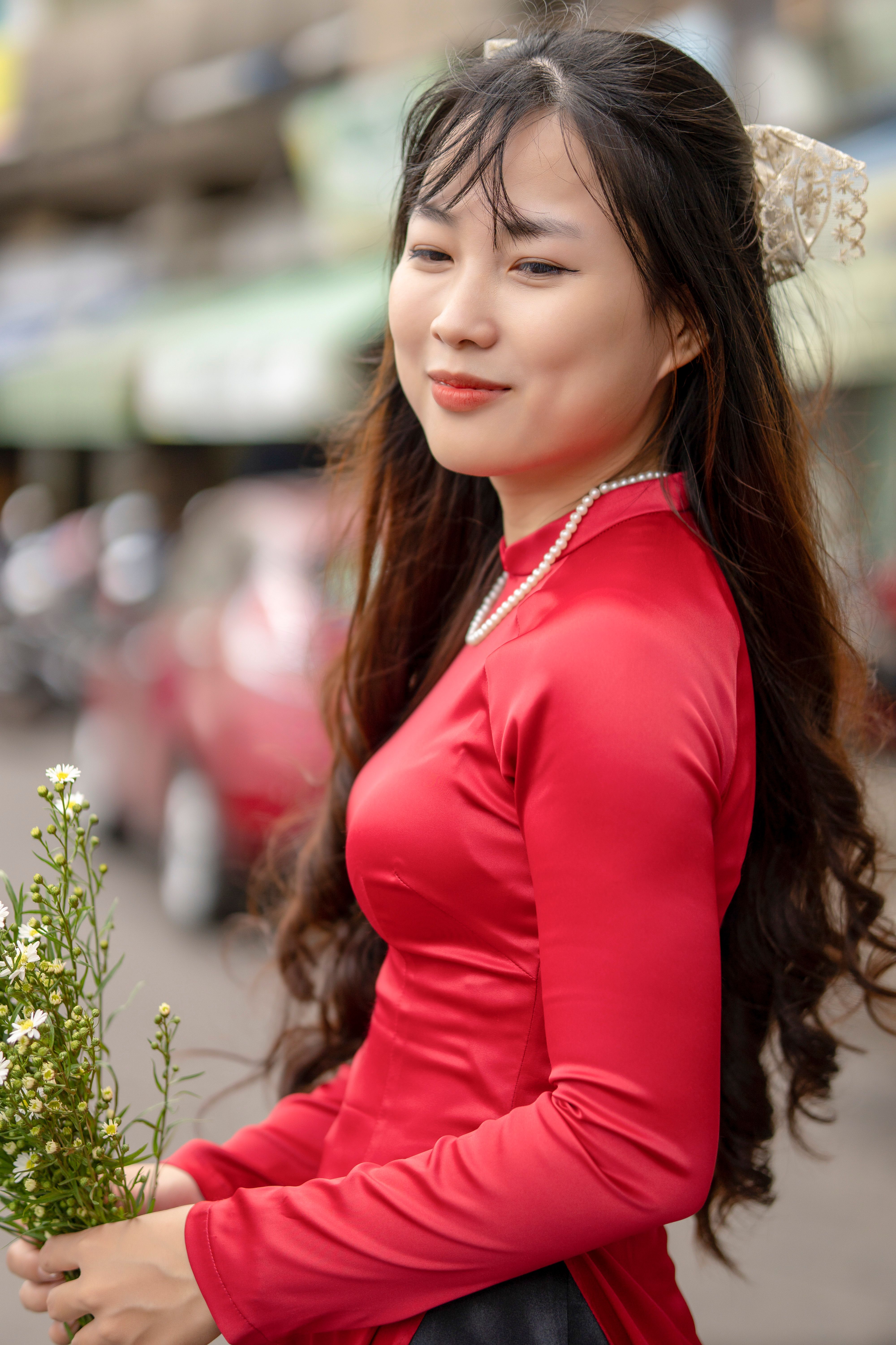 Beautiful young woman in a red dress smiling while holding flowers outdoors.