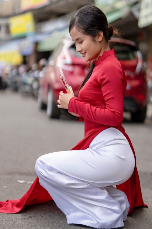 Free Smiling woman in a vibrant red dress kneeling on a city street, radiating elegance and charm. Stock Photo