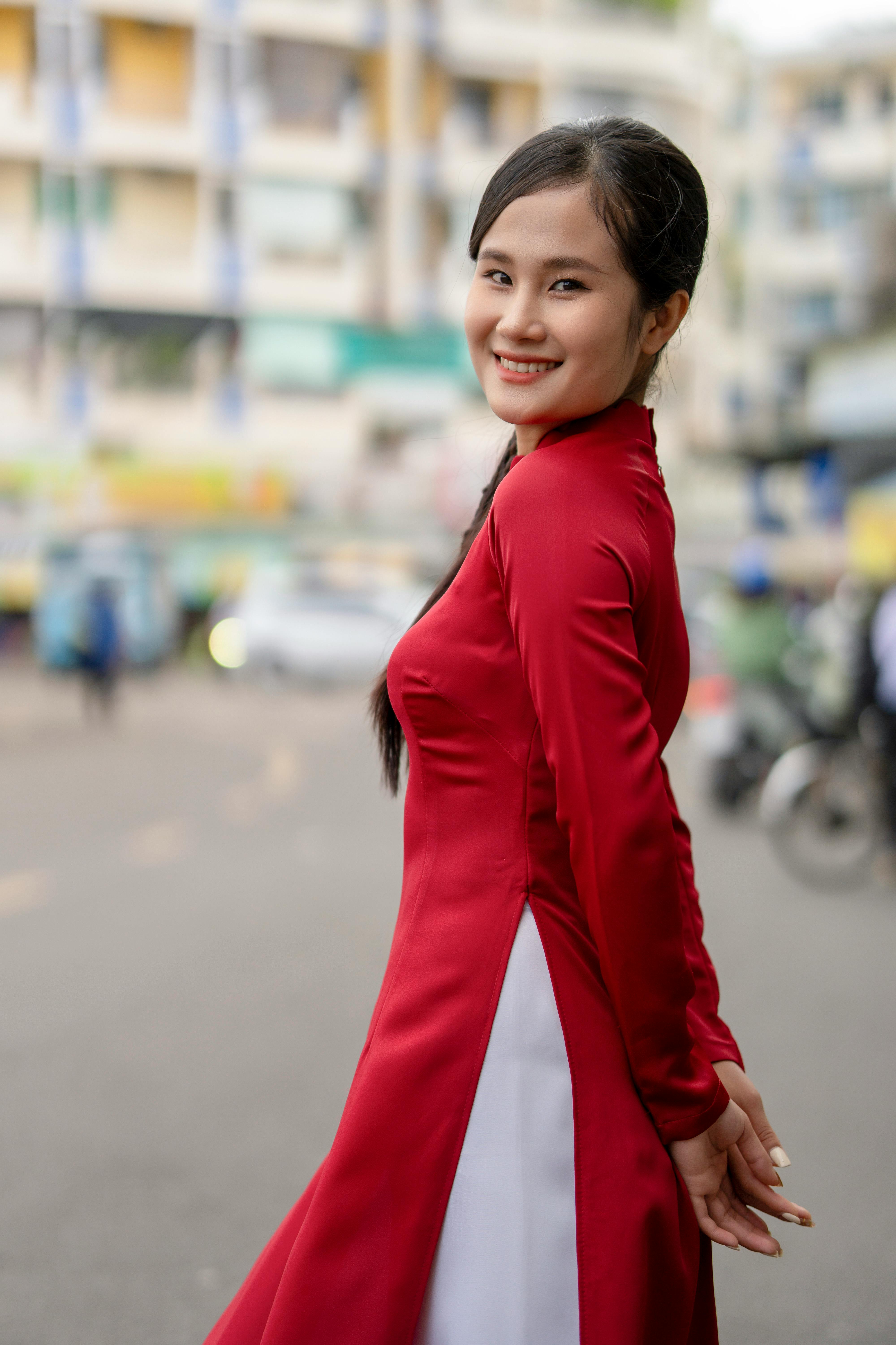 Smiling woman in a red traditional gown posing on an urban city street.