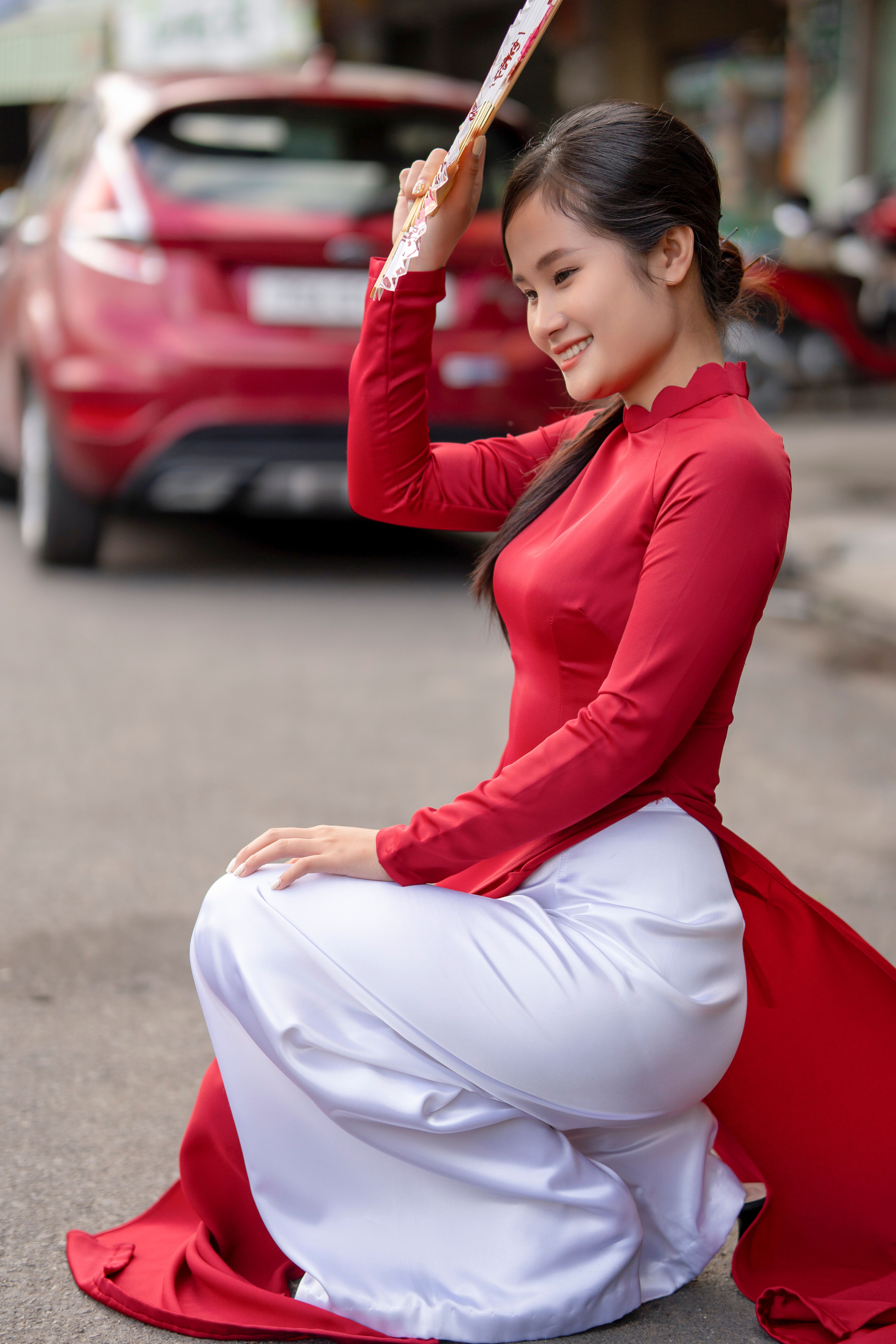 A smiling woman in a red traditional gown poses on a city street, exuding cultural elegance.