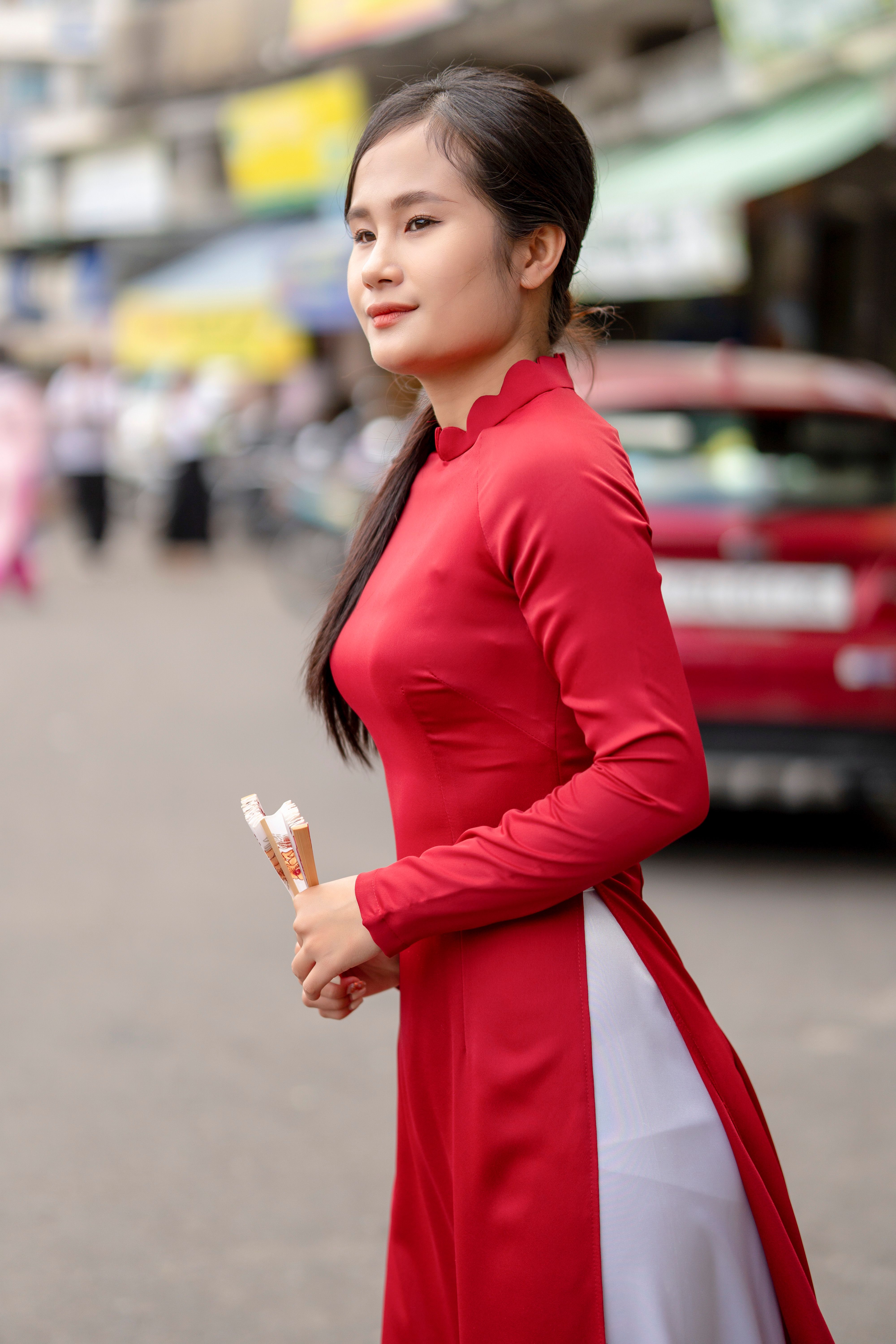 Profile of a woman in a red traditional gown walking along a bustling city street.