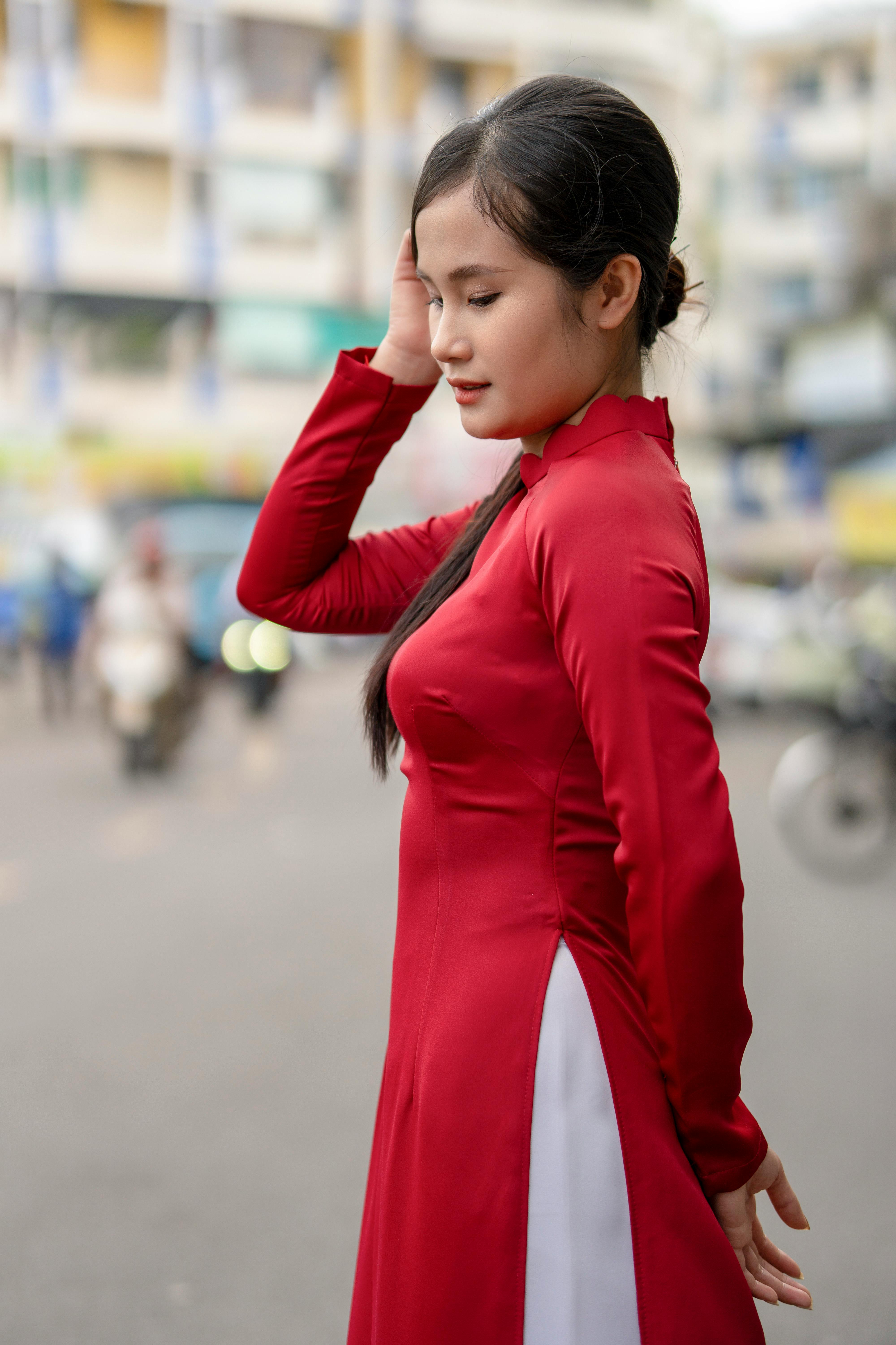 A fashionable woman in a red dress poses gracefully on a busy city street with blurred background.