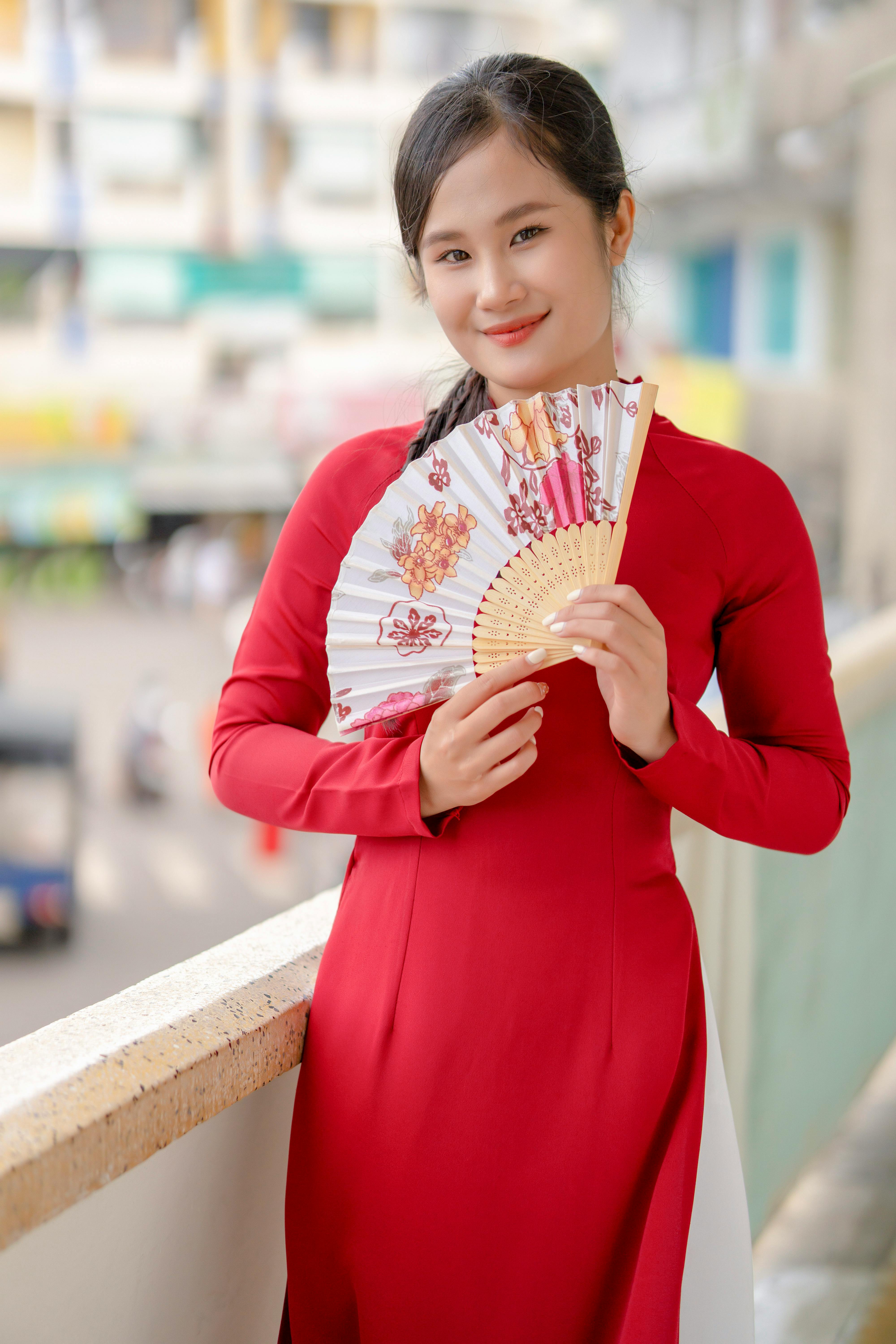 Portrait of a young woman in a red traditional Ao Dai holding a decorative fan.