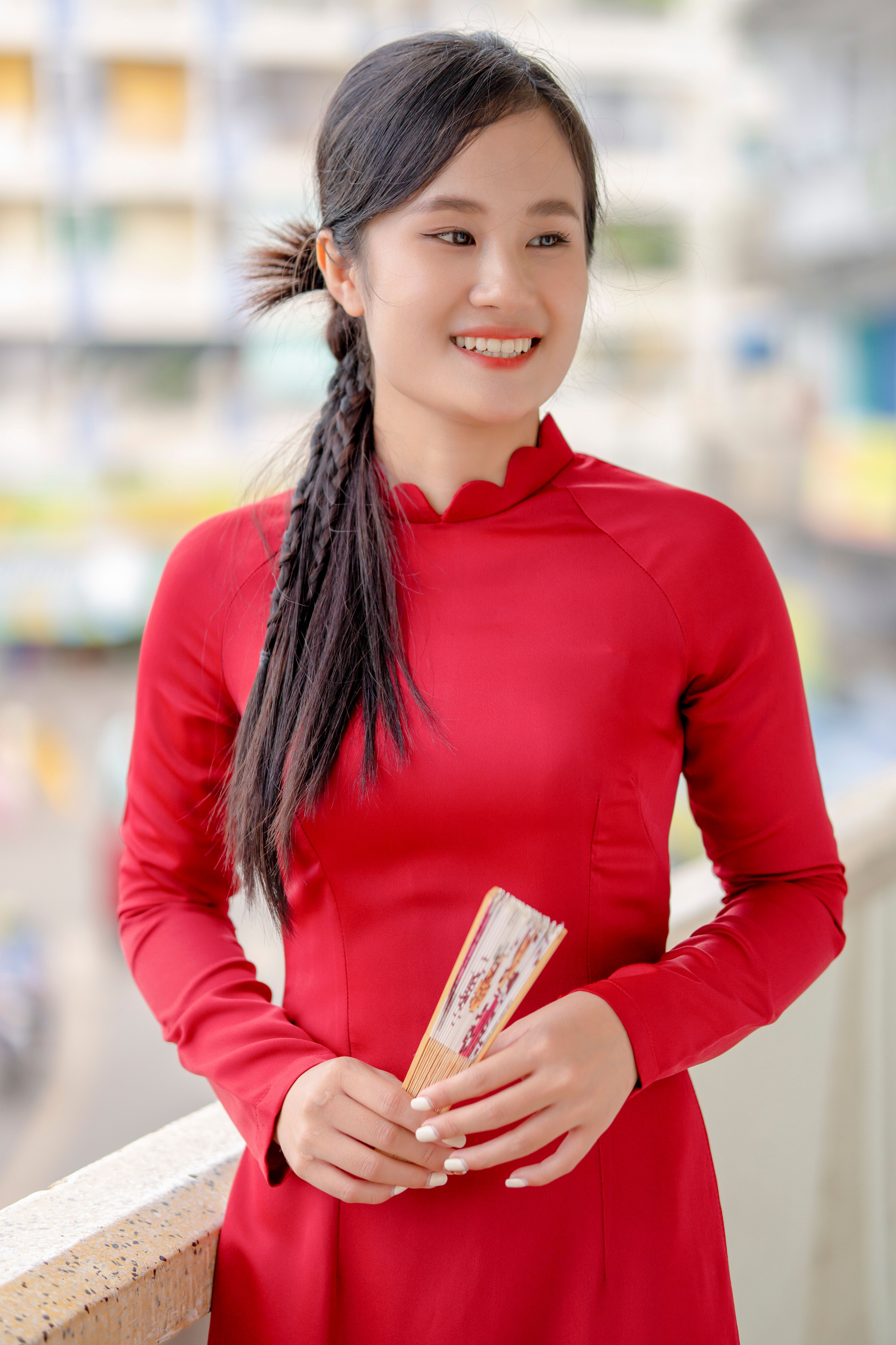 A young woman in a red dress smiles while holding a colorful bookmark.