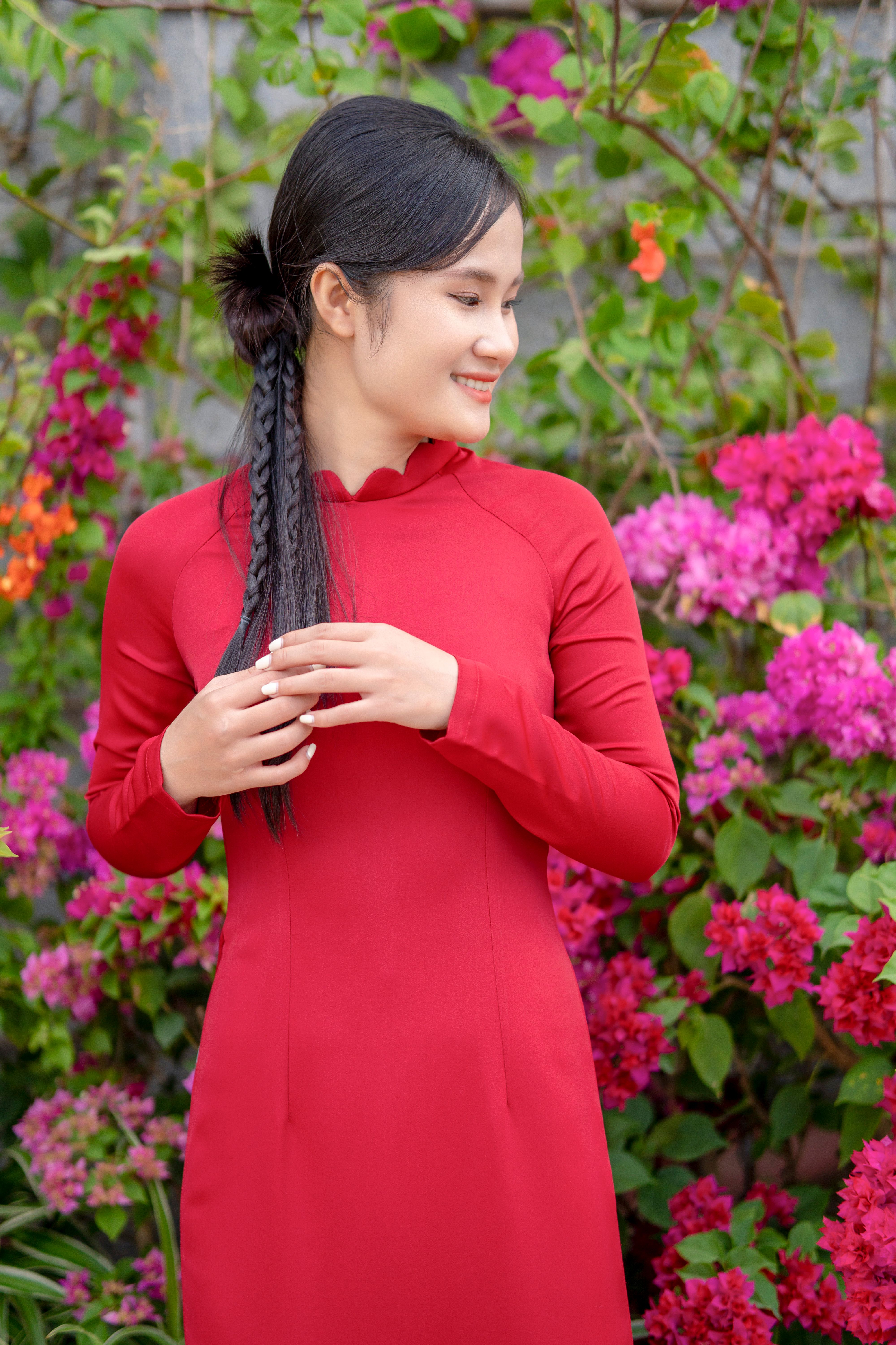 Smiling woman in a red dress surrounded by vibrant pink flowers outdoors.