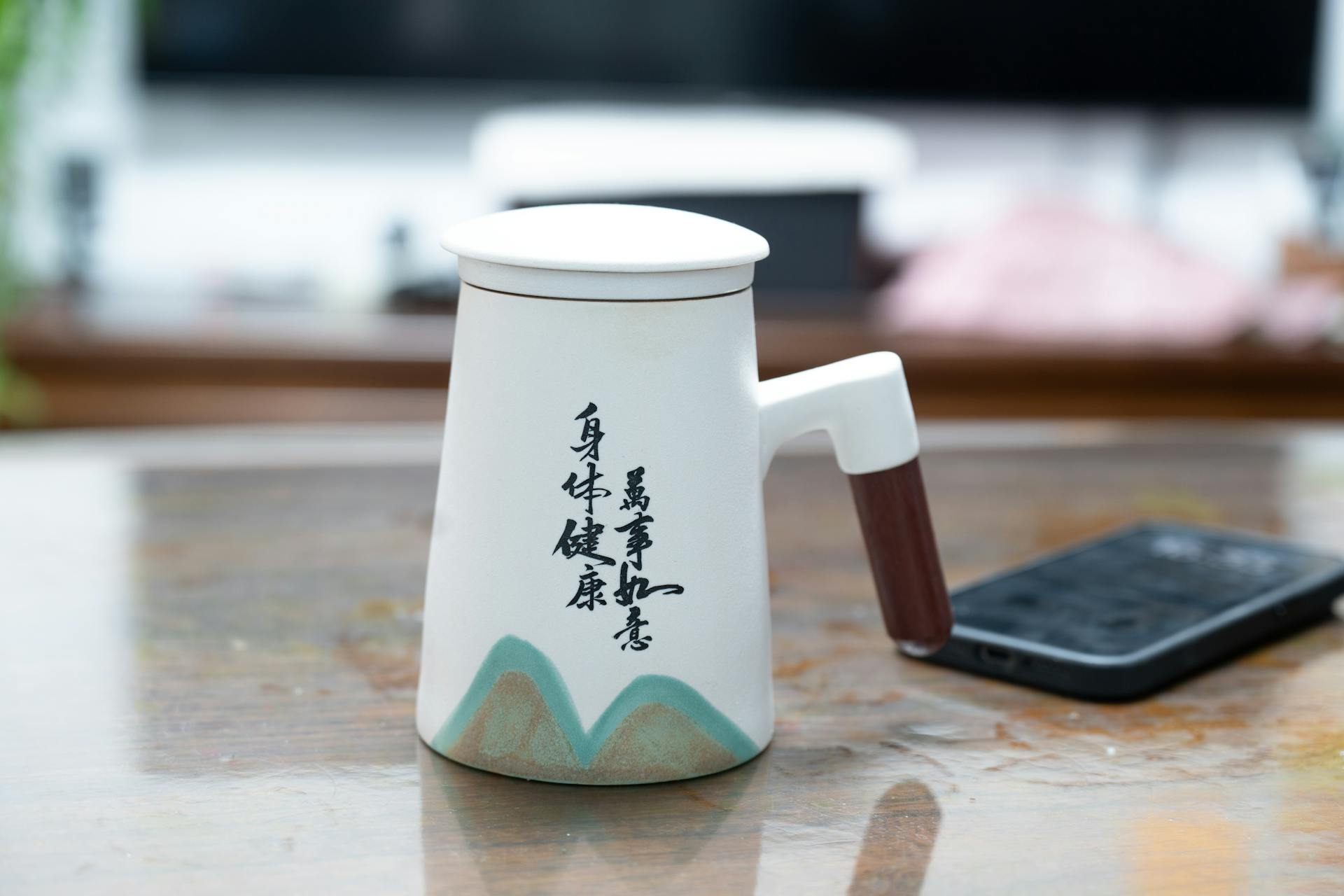 Oriental ceramic teapot with artistic Chinese calligraphy on a wooden table indoors.