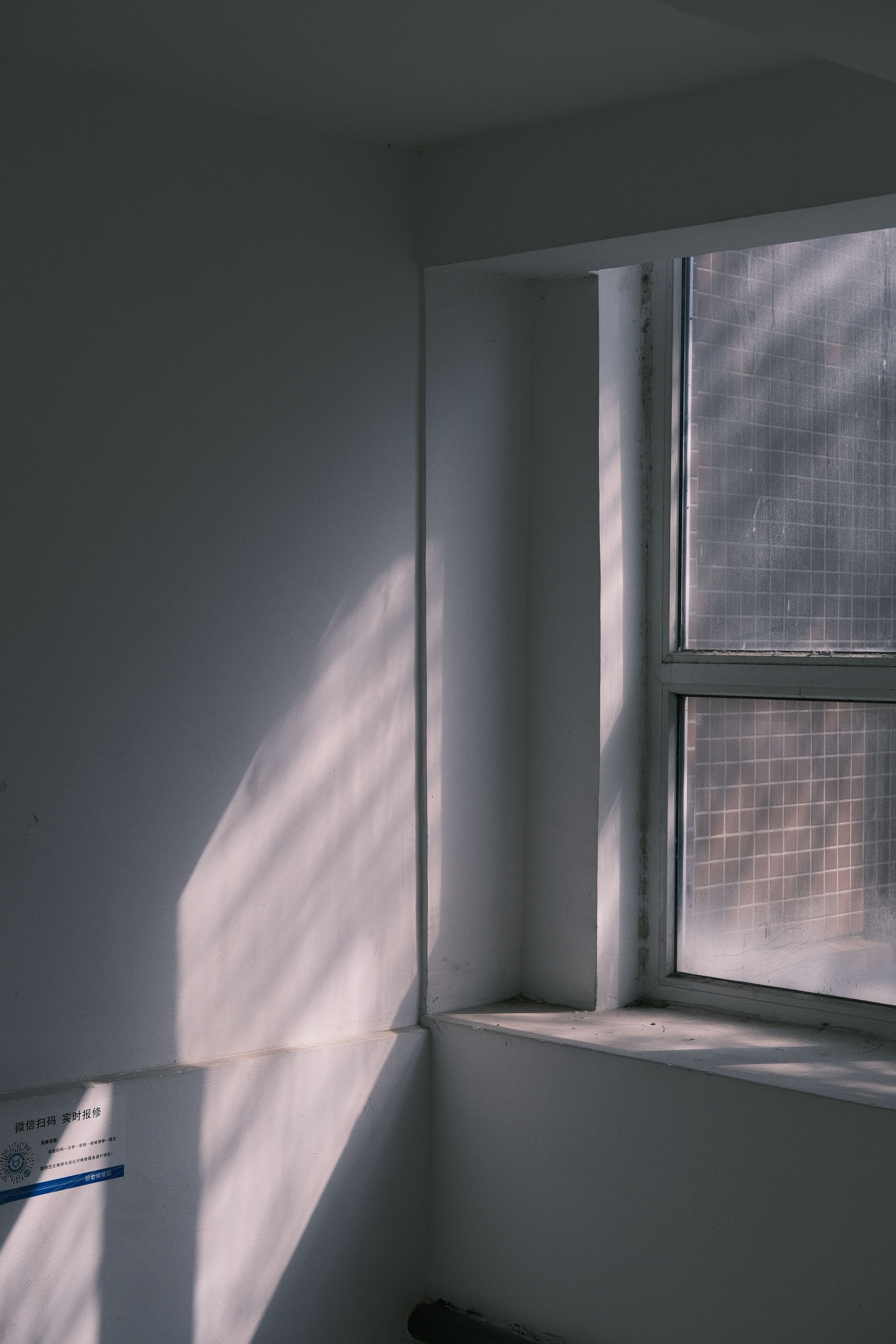 A minimalist white room featuring sunlight casting shadows through a window.