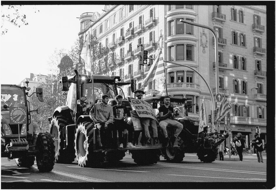 Imagen en blanco y negro de una protesta con personas en tractores en las calles de Barcelona.