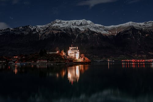 A castle on a lake at night with mountains in the background