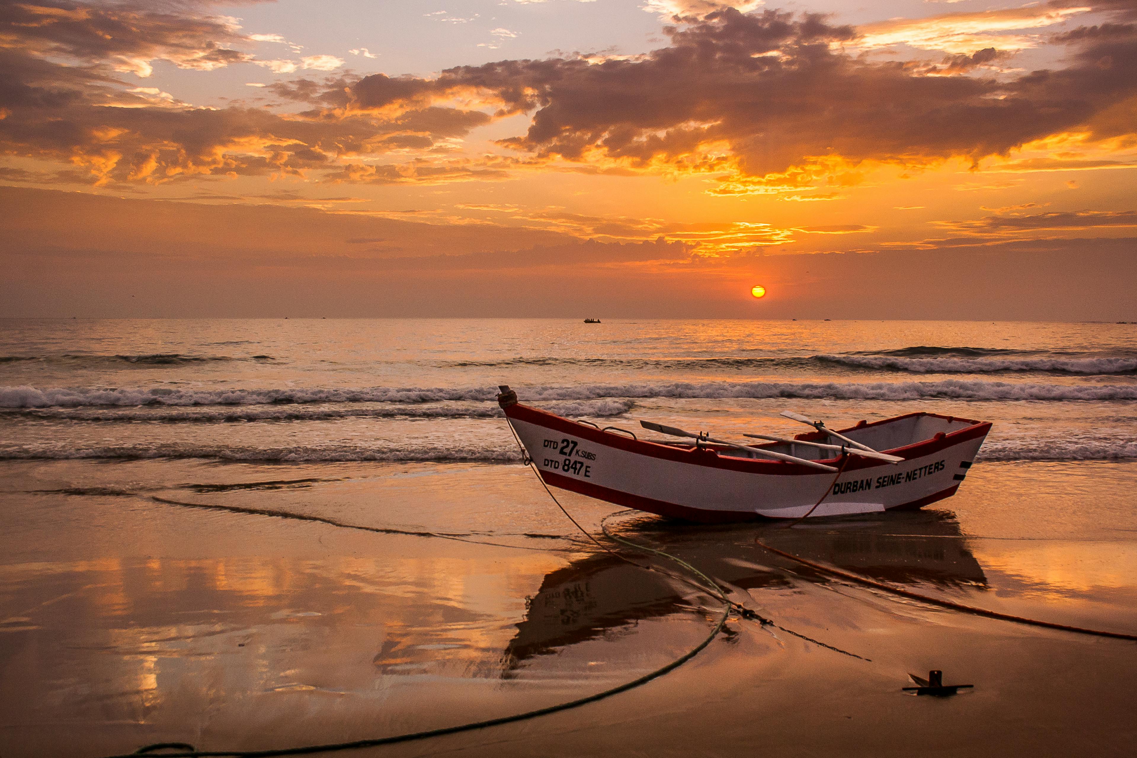Peaceful sunset over Durban beach with a rowboat on the sand reflecting the warm sky.