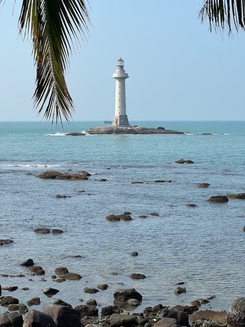 A lighthouse is seen in the ocean near palm trees