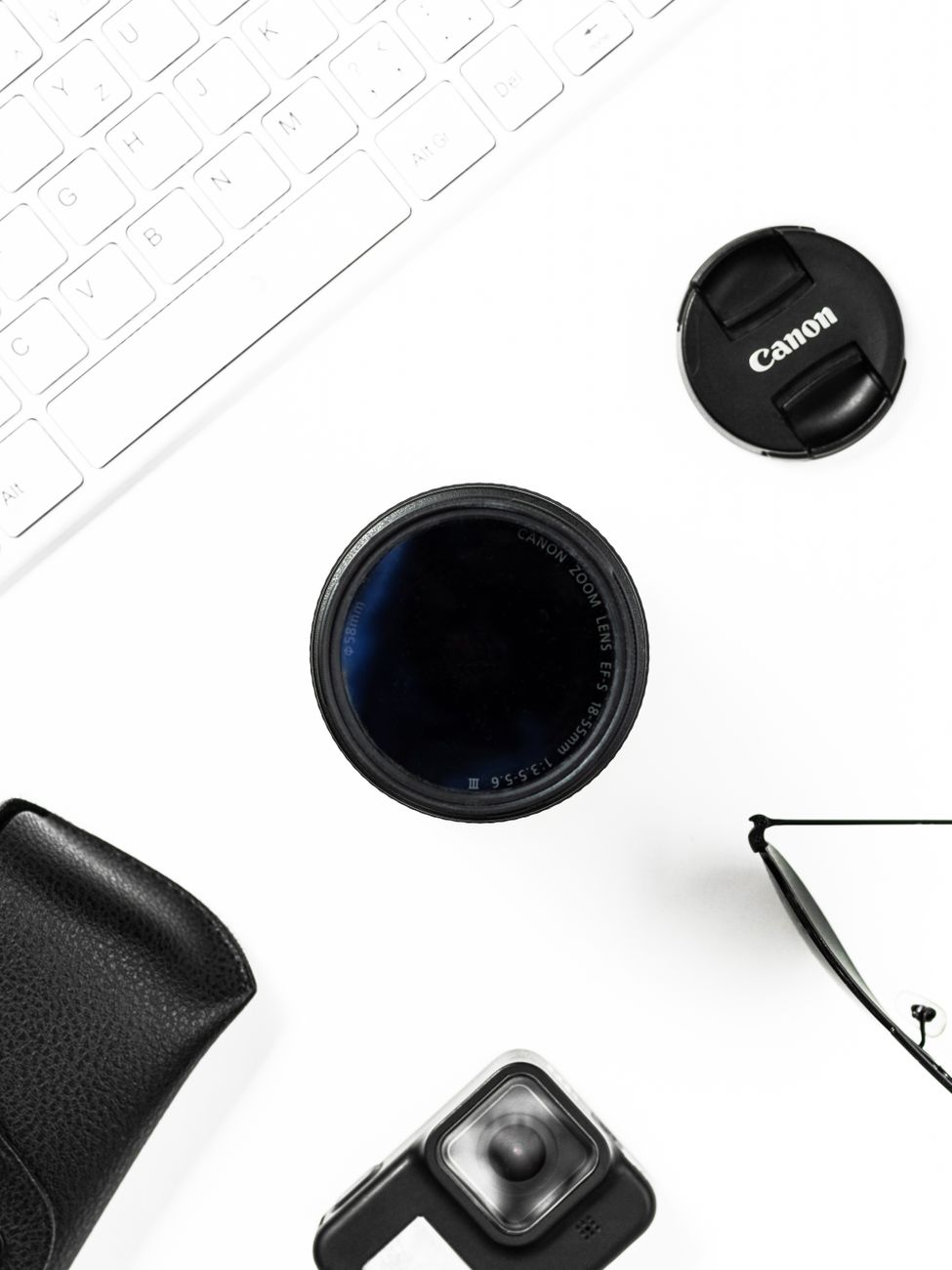 Flat lay of Canon lens, camera accessories, and keyboard on white background.. flat, canon, lens