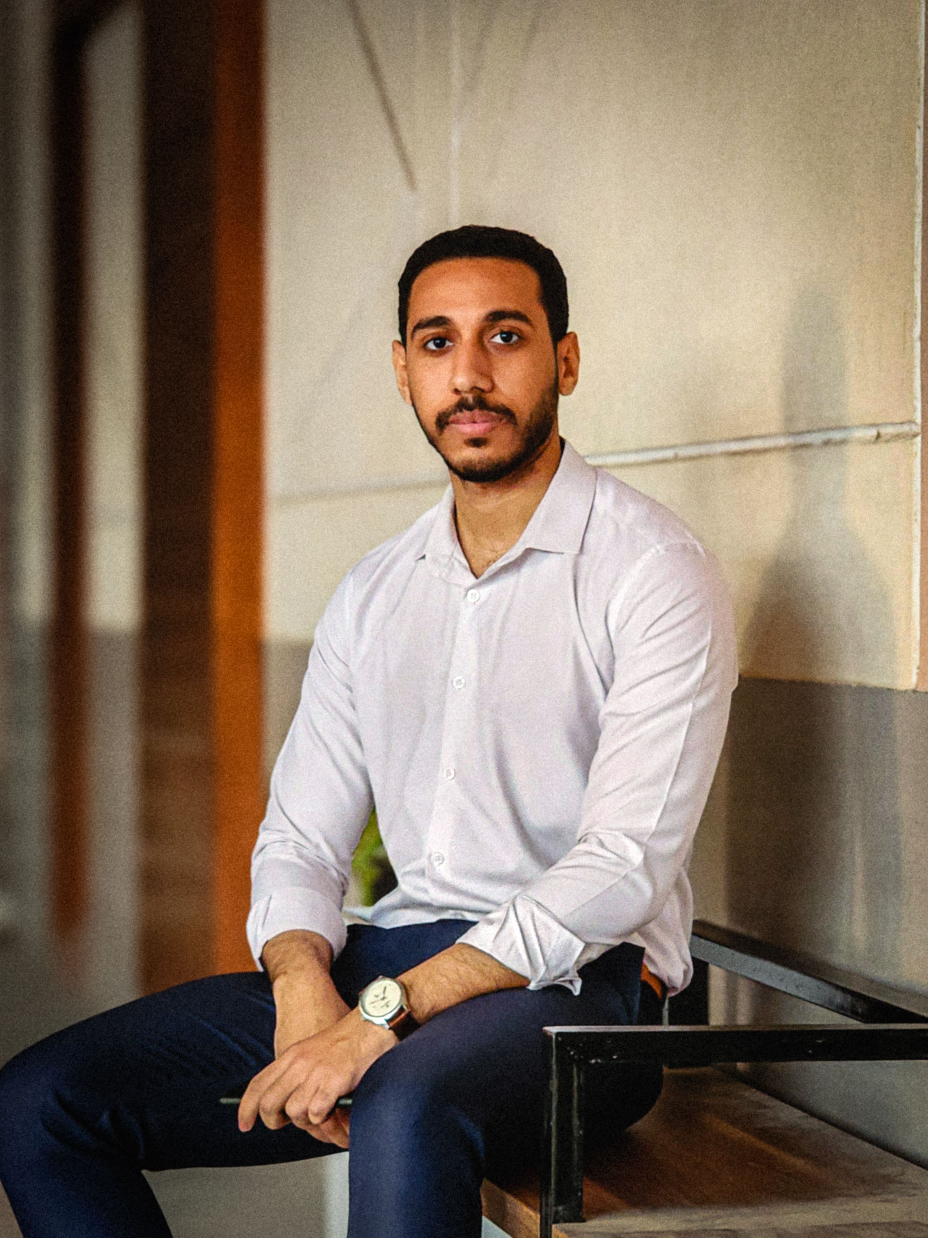 Stylish portrait of a young man in a white shirt sitting on a bench indoors.