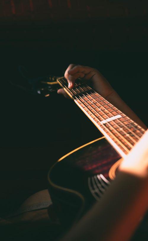 Free A moody close-up of a hand playing an acoustic guitar, captured in soft lighting. Stock Photo