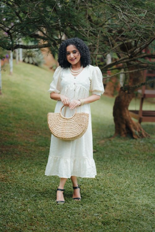 Free Young woman in a white dress posing with a straw bag in a lush green park in Thodupuzha, India. Stock Photo