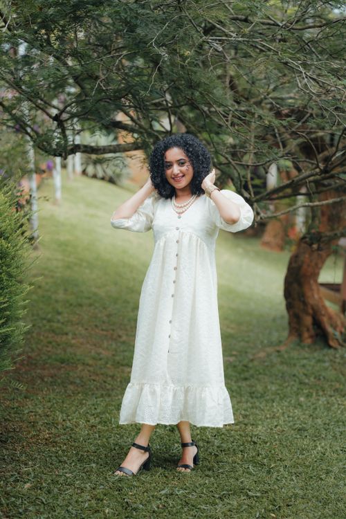 Free Graceful young woman with curly hair posing in a park setting wearing a white dress. Stock Photo