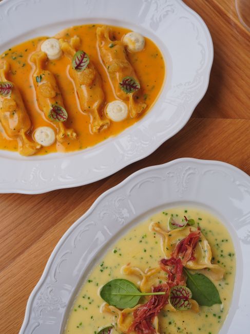 A white plate of golden butternut squash ravioli tossed in brown butter sauce, topped with crispy fried sage leaves and shaved Parmesan.