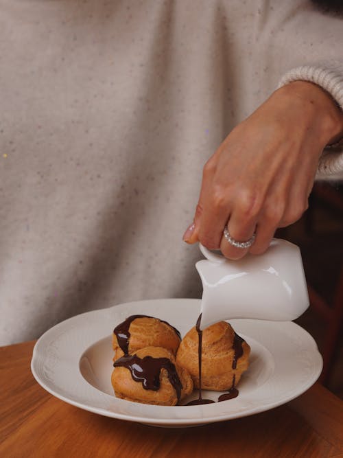 A person pouring milk on a plate with some pastries