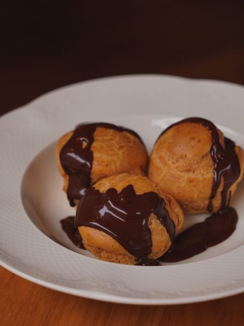 Free Savor the indulgence of creamy profiteroles topped with luscious chocolate sauce on a pristine plate. Stock Photo