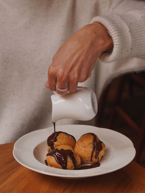 Free A hand pouring chocolate sauce over profiteroles, creating a delicious dessert. Stock Photo