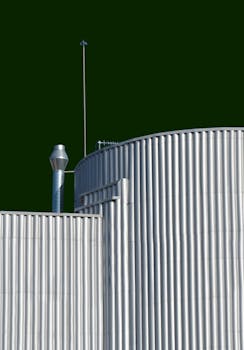 Cylindrical metal structures with chimney against a vibrant green sky, showcasing industrial design.