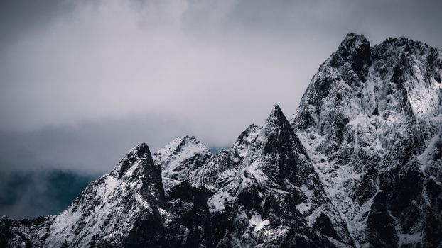 Dramatic view of rugged, snowcapped mountain peaks under cloudy sky.